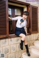 A woman in a school uniform leaning against a window.