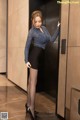 A woman in a blue top and black skirt standing in an elevator.