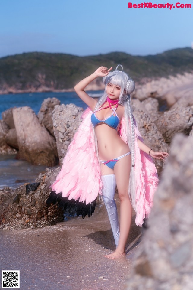 A woman in a bikini standing on a beach next to the ocean.