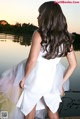 A woman in a white dress standing by a body of water.