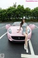 A woman sitting on top of a pink sports car.