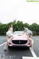 A couple of women sitting on top of a pink car.