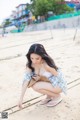 A woman in a blue and white dress crouching on a beach.